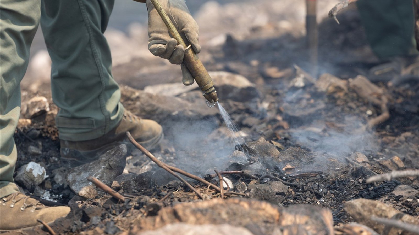 Brigadista forestal apagando un foco de incendio con una boquilla de bomba de espalda sobre terreno quemado